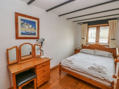 A bedroom with a wooden bed and dresser with a mirror at Cowslip Cottage in Rosemarket
