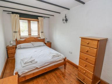 A bedroom with a wooden bed white bedding wooden dresser and window with curtains at Cowslip Cottage in Rosemarket
