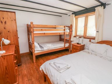 A bedroom with bunk beds a double bed wooden furniture and a window with blinds at Cowslip Cottage in Rosemarket