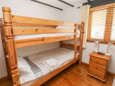 A bedroom with wooden bunk beds and a wooden nightstand with two lamps and a device by a window at Cowslip Cottage in Rosemarket