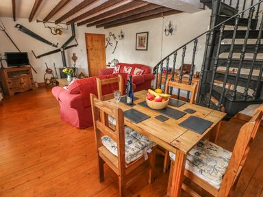 A dining and living area with a wooden table and chairs a red sofa and a black spiral staircase at Primose Cottage in Rosemarket