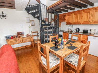 A kitchen and dining area with wooden furniture a spiral staircase and kitchen appliances at Primose Cottage Rosemarket