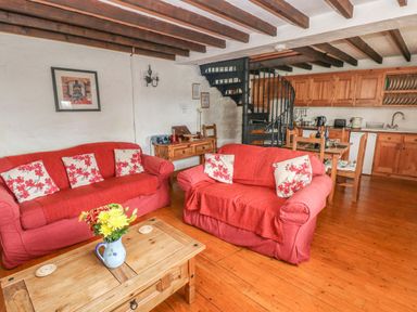 A living room with two red sofas a wooden coffee table with flowers and a kitchen with wooden cabinets at Primose Cottage in Rosemarket