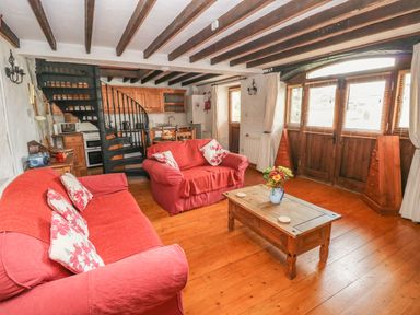 A living room with red sofas a wooden coffee table and a spiral staircase at Primose Cottage in Rosemarket