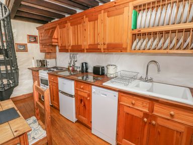 A kitchen with wooden cabinets a white sink a dishwasher a refrigerator a stove and a black spiral staircase at Primose Cottage in Rosemarket