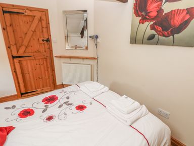 A bedroom with a wooden door a bed with floral bedding a mirror and a hairdryer on the wall at Primose Cottage in Rosemarket