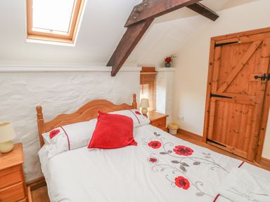 A bedroom with a wooden bed and floral bedding under a slanted ceiling with a skylight at Primose Cottage Rosemarket
