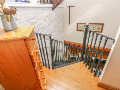 A wooden staircase with black metal railings next to a wooden chest of drawers at Primose Cottage in Rosemarket