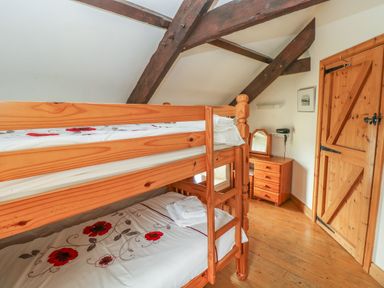 A bedroom with wooden bunk beds a small dresser with mirror and wooden door at Primose Cottage in Rosemarket