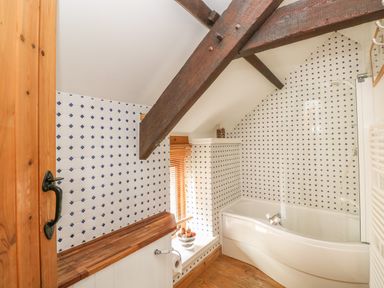 A bathroom with wooden beams a bathtub with a glass screen tiled walls and a wooden door at Primose Cottage in Rosemarket