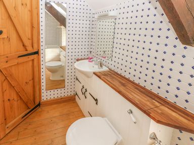A bathroom with wooden floor a wooden door a toilet sink with wooden countertop and blue and white tiled walls at Primose Cottage in Rosemarket