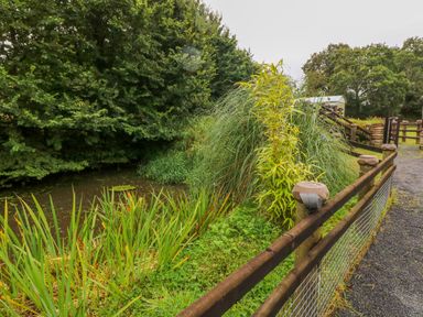 A fenced gravel path next to water and dense vegetation at Shepherds Hut - The Crook in Rosemarket near Neyland