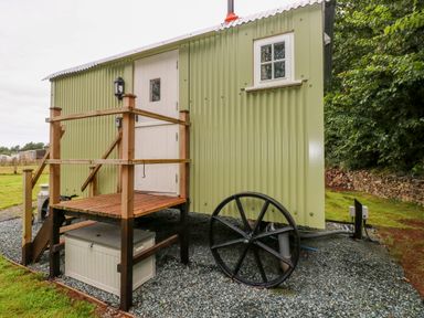 An exterior view of a green shepherds hut with wooden steps and black wheels at Shepherds Hut - The Crook in Rosemarket near Neyland