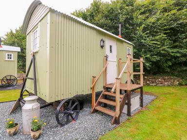 A shepherds hut with steps and railing outside surrounded by grass and trees at Shepherds Hut - The Crook in Rosemarket near Neyland