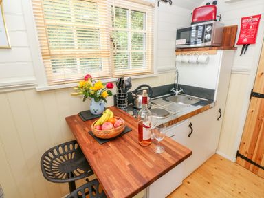 A small kitchen area with a wooden countertop a fruit basket a bottle of wine and two glasses a microwave a sink and kitchen utensils at Shepherds Hut - The Crook in Rosemarket near Neyland