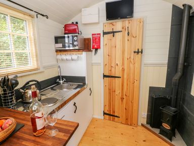 A kitchen area with a sink microwave red toaster wood stove wooden door and bottle with wineglass at Shepherds Hut - The Crook Rosemarket near Neyland