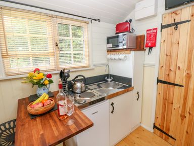 A small kitchen with a wooden countertop a sink a kettle a microwave a fruit basket and a bottle of wine at Shepherds Hut - The Crook Rosemarket near Neyland