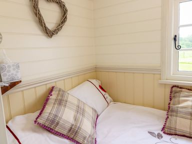 A small bedroom corner with a bed two plaid pillows and a window at Shepherds Hut - The Crook Rosemarket near Neyland