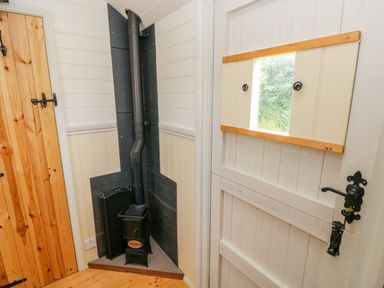 A corner with a small black wood stove and a white wooden door with a small window at Shepherds Hut - The Crook Rosemarket near Neyland