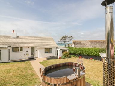 A backyard with a wooden hot tub and drinks near a white house with a sea view at Chi An Mor in Porth
