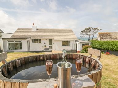 An outdoor hot tub with two glasses of rose wine and a bottle in a cooler in a garden with a white house in the background at Chi An Mor in Porth