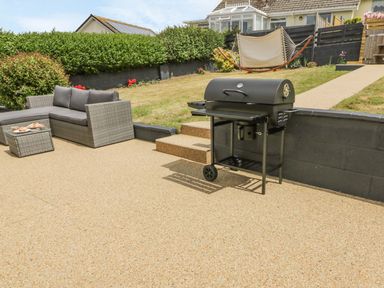 An outdoor patio with a barbecue grill a wicker sofa and a hammock in a garden at Chi An Mor in Porth