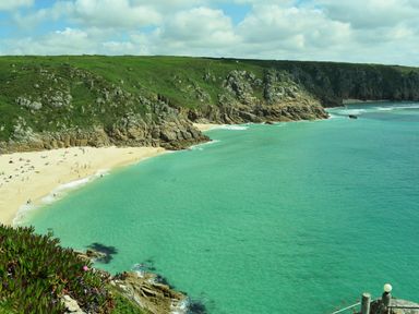 A sandy beach with people next to turquoise sea and rocky cliffs with green grass at Chi An Mor in Porth