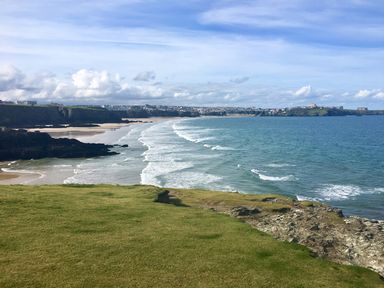 A coastal landscape with grassy cliffs overlooking a sandy beach and ocean waves at Chi An Mor in Porth