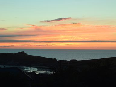 A sunset over the ocean with a silhouette of cliffs and land at Chi An Mor in Porth