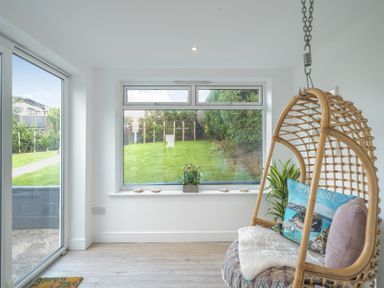 A conservatory with a hanging chair and a view of the garden at Chi An Mor in Porth