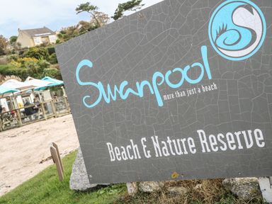 A sign for Swanpool Beach and Nature Reserve with outdoor seating and a house in the background at Phenests in Falmouth
