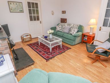 A living room with a green couch a glass coffee table on a red rug and a wooden armchair at Phenests in Falmouth