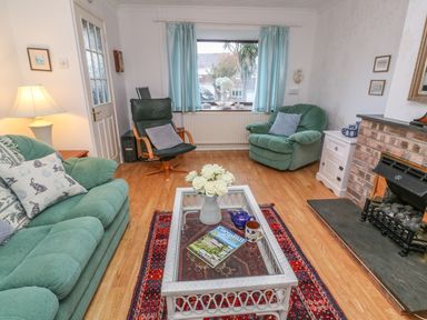 A living room with green armchairs a wooden coffee table with flowers and magazines a fireplace and a window with blue curtains at Phenests in Falmouth