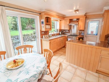 A kitchen with wooden cabinets a round dining table with fruit on it and glass doors leading outside at Phenests in Falmouth