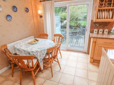 A kitchen dining area with a round table covered by a cloth and surrounded by wooden chairs next to sliding glass doors opening to an outdoor patio at Phenests in Falmouth