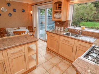 A kitchen with wooden cabinets and granite countertops a dining table with chairs and wall decor near sliding glass doors at Phenests in Falmouth