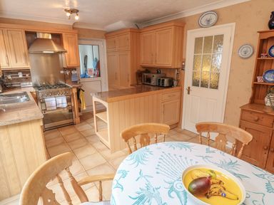 A kitchen with wooden cabinets a round table with fruit a stove and a microwave at Phenests in Falmouth