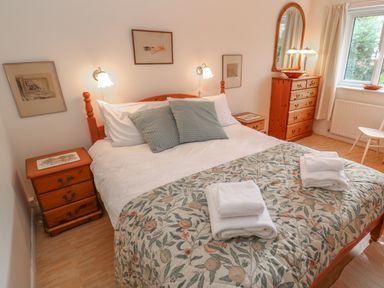 A bedroom with a bed with pillows and folded towels two bedside tables a chest of drawers with mirror and a window at Phenests in Falmouth