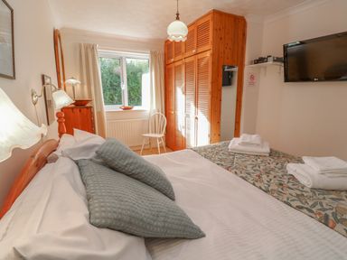 A bedroom with a double bed pillows and towels a wooden wardrobe a white chair and a wall-mounted television at Phenests in Falmouth