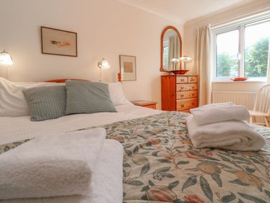 A bedroom with a bed, pillows, folded towels, wooden dresser with mirror, and a window at Phenests in Falmouth
