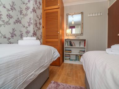 A bedroom with two beds white linens wooden wardrobe bookshelf with books and a mirror at Phenests Falmouth