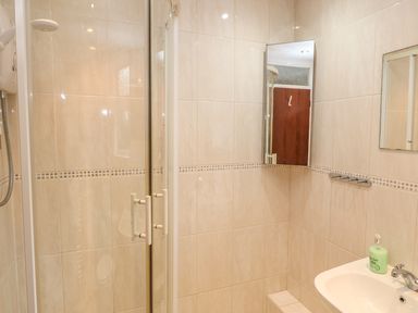 A bathroom with a glass shower enclosure a wall-mounted mirror a sink with a faucet and a soap dispenser at Phenests in Falmouth