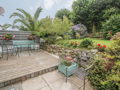 An outdoor patio with metal chairs and a wooden bench next to a garden with flowers and greenery at Phenests in Falmouth