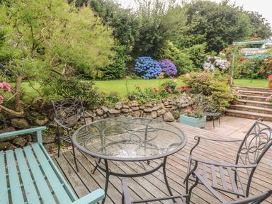 A garden patio with metal chairs a glass table a wooden bench flowers and stone steps at Phenests in Falmouth