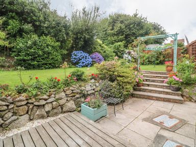 A garden with stone steps, a metal chair, flower pots, and a trellis at Phenests in Falmouth