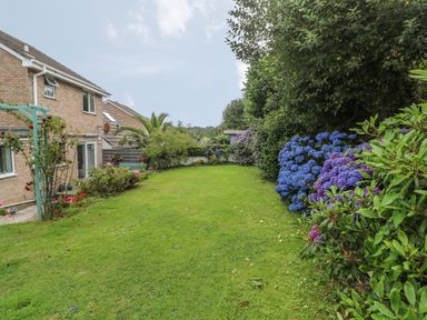 A backyard garden with green lawn and flowering shrubs next to a brick house at Phenests in Falmouth
