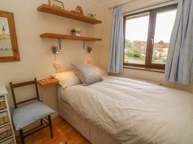 A bedroom with a bed next to a window with blue curtains a wooden chair with a blue cushion and wooden shelves on the wall at Phenests in Falmouth