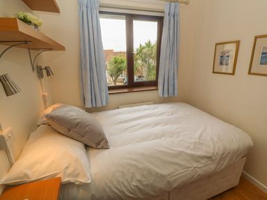A bedroom with a double bed near a window with blue curtains and framed pictures on the wall at Phenests in Falmouth