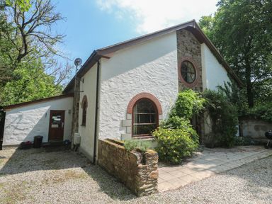 A white stone house with arched windows surrounded by greenery and a gravel driveway at Beggars Roost in Penhallow