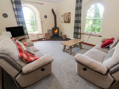 A living room with two sofas a wooden coffee table a wood burning stove and a television at Beggars Roost in Penhallow